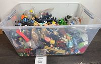 Transparent plastic bin filled with assorted small figures and toys in used condition.