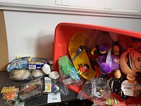 Photo showing large red plastic bin with various toys including plush figures, yellow toy truck and other small toys inside bin and around it.