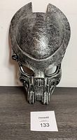 Front view of silver-toned metal Predator mask with detailed sculpting of eyes, mouth, and forehead.