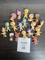 Overhead photo showing 18 Twozies baby animal figures arranged on dark surface with MaxSold auction card in frame.