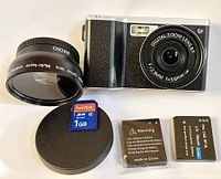 Camera with macro lens, 1GB SD card, two lithium-ion batteries, and lens covers, all laid out on a white surface.