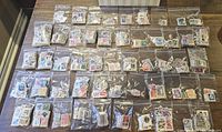 Packets of multiple small plastic bags filled with used postage stamps, laid out in rows on a table showing many stamps from various countries.