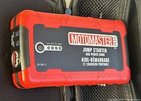 Close-up of Motomaster branded jump starter and power bank device showing the power button, battery indicator LEDs and USB ports on side.