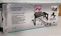 Photo of product box depicting the laptop stand with product details and photos of the product in use on bed and table.