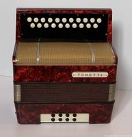 Front view showing the red and black marbled finish, melody button keys, metallic grille, and bass side buttons.