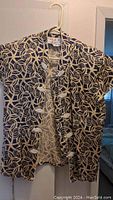 Black and beige Chinese style top hanging on a hanger, clearly showing the patterned design and style features.