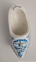 Front of a white ceramic shoe wall hanging with blue hand-painted windmill and floral patterns, labeled 'Holland'.