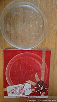 Photo showing a clear crystal platter placed on top of its original red colored box with a Christmas theme design.