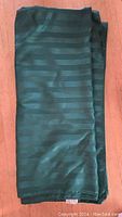 Folded green tablecloth showing its striped design and fabric texture on a wooden surface.