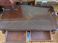 Top view of coffee table showing glass top and wood inlay design underneath, with two drawers partially open.
