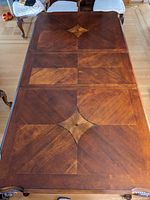 Top view of solid wood dining table showing detailed wood grain pattern with diamond and fan shaped inlay motifs on the tabletop.