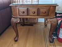 Front view of one side table showing three drawers with wooden knob pulls and ornate carved cabriole legs.