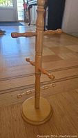 Photo of the wooden jewelry rack standing on a wood floor, showing the vertical column with four pairs of horizontal pegs and round base.