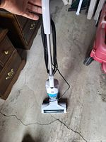 Full white and blue Bissell 3-in-1 vacuum cleaner standing upright on concrete floor, held by handle