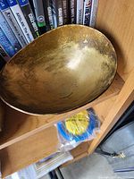 Photo of a brass bowl placed on a wooden shelf with various DVDs and items in the background.
