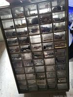 Front view of beige plastic organizer case with multiple small transparent drawers containing nails, screws, and hardware.