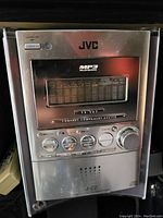 Front view of a silver JVC compact component system showing control buttons, volume knob, and 5-CD changer with MP3 playback label.