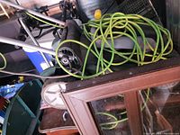 Top and side view of electric lawnmower showing green and black body, wheels and green power cord.
