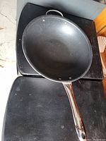 Top-down view of a large black non-stick frying pan with a long metallic handle and three rivets attaching the handle.