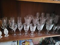 Shelf display of assorted clear crystal glassware and a decorative glass pineapple figurine.