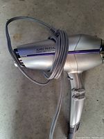 Silver John Frieda hair dryer with cord wrapped around the handle shown from side.