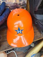 Photo of an orange hard helmet with blue star and 'H' logo on the front showing surface scratches.