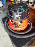 Henry vacuum cleaner showing black top with controls and orange body with face and attached flexible hose.