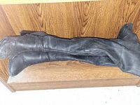 Pair of long black boots laid flat on wooden surface, showing length and shape.