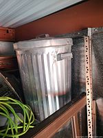 Metal trash can with a lid placed inside a storage area showing its side and lid handles.