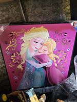 Square wall art photo showing Elsa and Anna from Disney Frozen hugging on a pink floral decorative background.