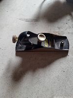 Photo of a black handheld metal bench planer with a brass adjustment knob and blade.