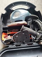 Electric palm sander with power cord, auxiliary handle, and sanding pad in carrying case.