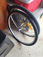Two bicycle wheels with tires leaning against a red cooler and wooden surface. One wheel has a yellow reflector attached to the spokes.