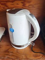 White electric kettle with water level indicator and power switch on handle, placed on a wooden surface.