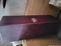 Photo showing rectangular dark brown wooden box with metal clasp on front for closing.