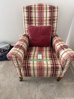 Front view of plaid armchair with red cushion on seat, fabric shows red, cream, and green plaid pattern.