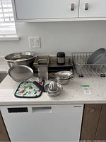 Photo showing all items on a kitchen counter including mixing bowls, baking pans, grater, sieve, pot holder, citrus juicer, and cooling rack.