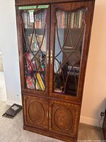 Full front view of the large wooden china cabinet with glass doors, filled with books.
