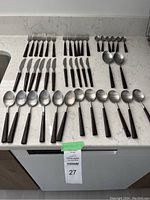 Full set of cutlery pieces arranged on countertop including forks, knives, spoons, and two cutlery holders.