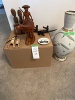 Lot showing large ceramic vase with floral design and various wooden carvings on a cardboard box