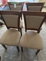 Top-front view showing four dining chairs arranged together, highlighting beige upholstered seats and backs with wood frames.