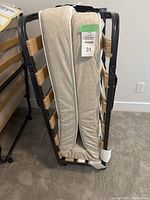 Folding bed frame folded in half with mattress attached, showing beige patterned mattress and wooden slats on metal frame.