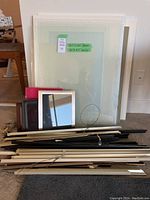 Image showing stacked clear glass sheets with taped size labels and various metal framing hardware pieces stacked in front, with cardboard pieces visible