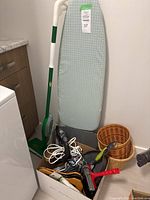 Overall view showing ironing board, mop, baskets, cleaning tools, and iron box.