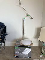 Full view of the silver adjustable arm floor lamp with tag tied in green tape, standing next to a box containing the color changing flush mount lights.