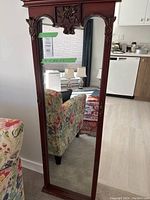 Full view of the large full-length mirror showing the wooden carved frame, floral carving detail at the top, and the reflective surface.