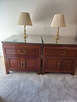 Two nightstands side by side with glass tops and brass lamps