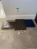 Three albums on carpeted floor with a small sealed bag of stamps in front. Albums include a brown Caperns Bird Album, a black album, and a blue album.