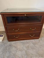 Front view of the wooden TV cabinet with glass top and two brass-pulled drawers.