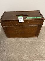 Closed oak-tone wooden chest with handle and M&W logo on front
